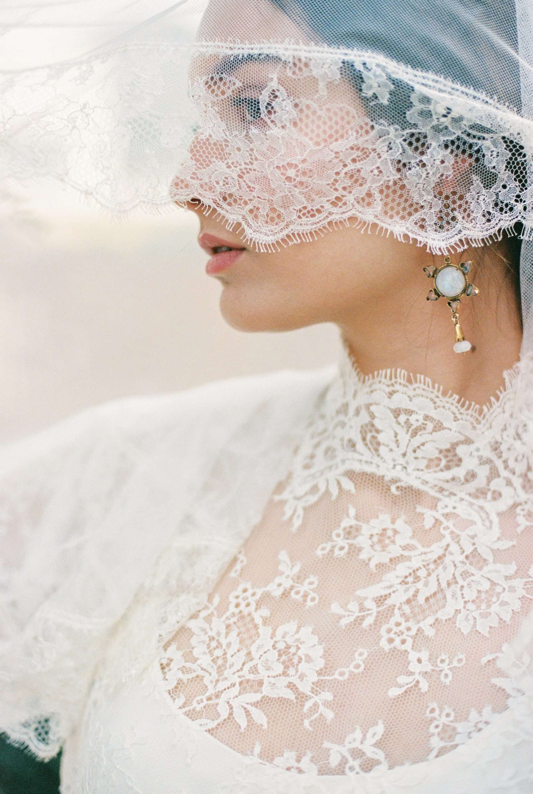 Profile picture of a bride. She's covering half her face with her veil and we can see her vintage earring.