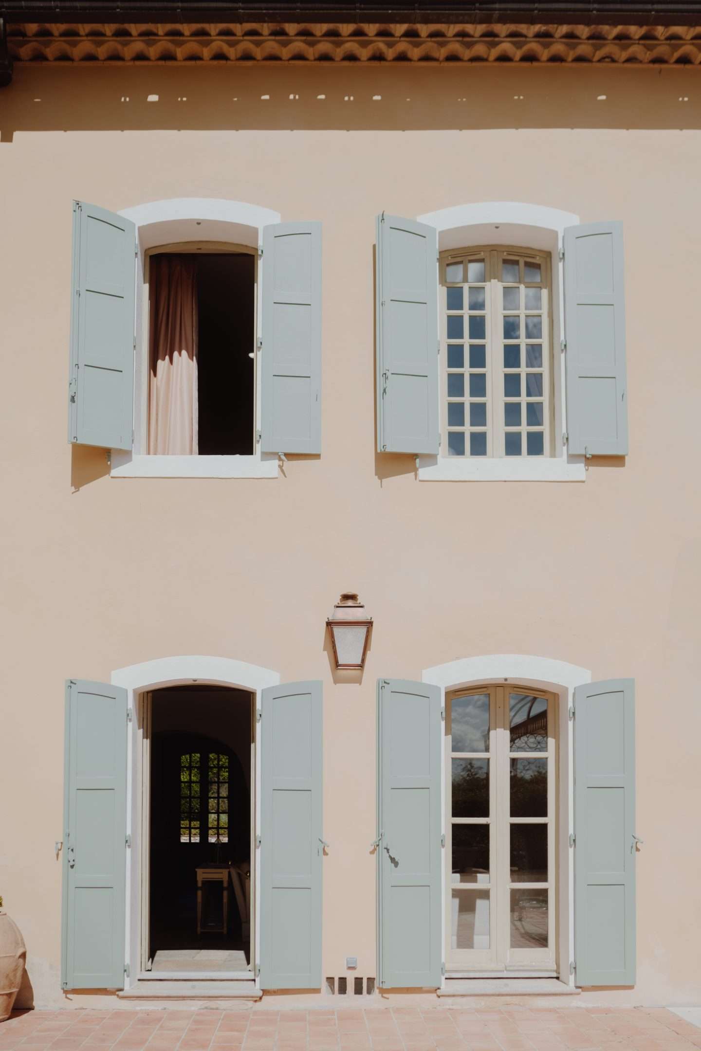 Four green windows in peach house. Two are open and two are closed.